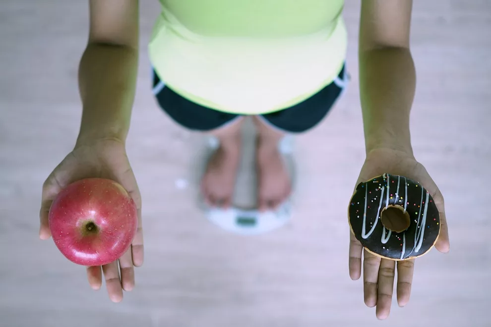 Women are weighing with scales, holding apples and donut. The decision to choose junk food that is not good for health and fruits that are high in vitamin C is good for the body. Diet concept